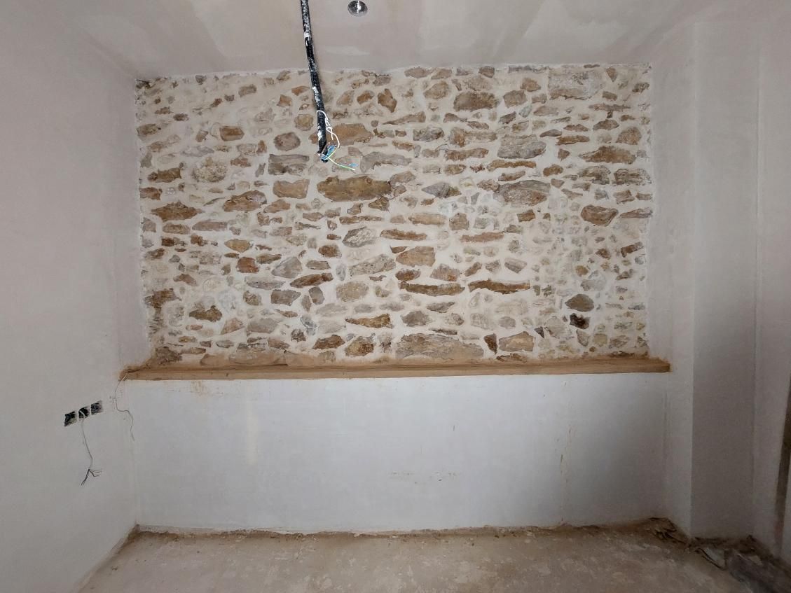 Habitación interior con pared de piedra vista, paredes blancas y repisa de madera.