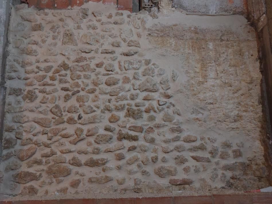 Muro de piedra parcialmente recubierto con mortero claro. Secciones con piedras expuestas.
