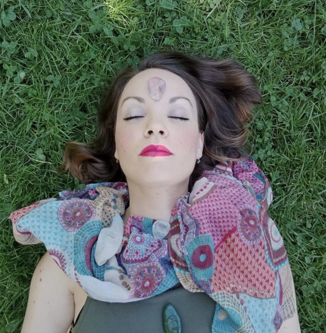 Una mujer está tumbada en la hierba con los ojos cerrados y una bufanda alrededor del cuello.