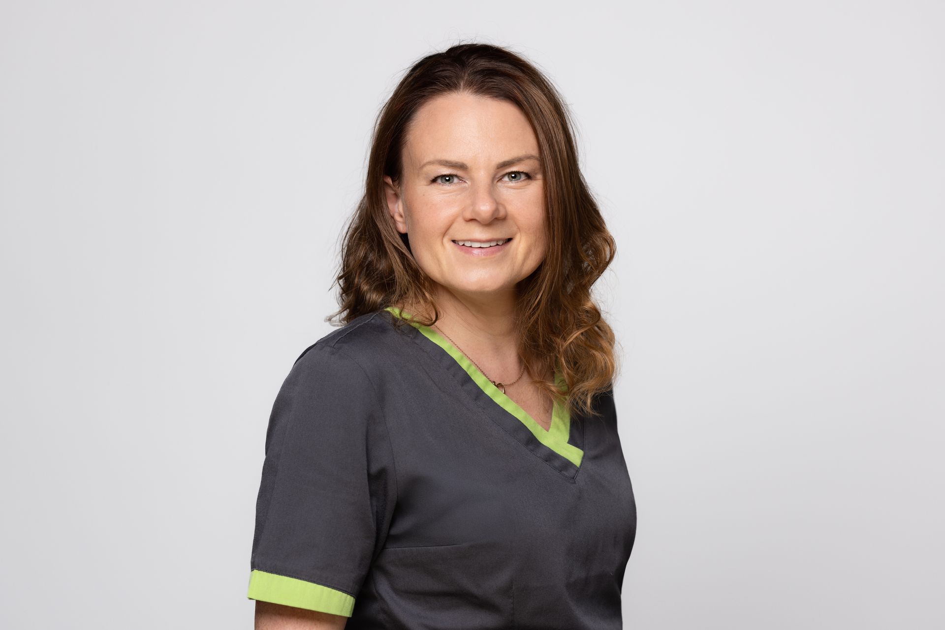 Eine Frau in einem grauen Kasack mit grünem Kragen lächelt in die Kamera.