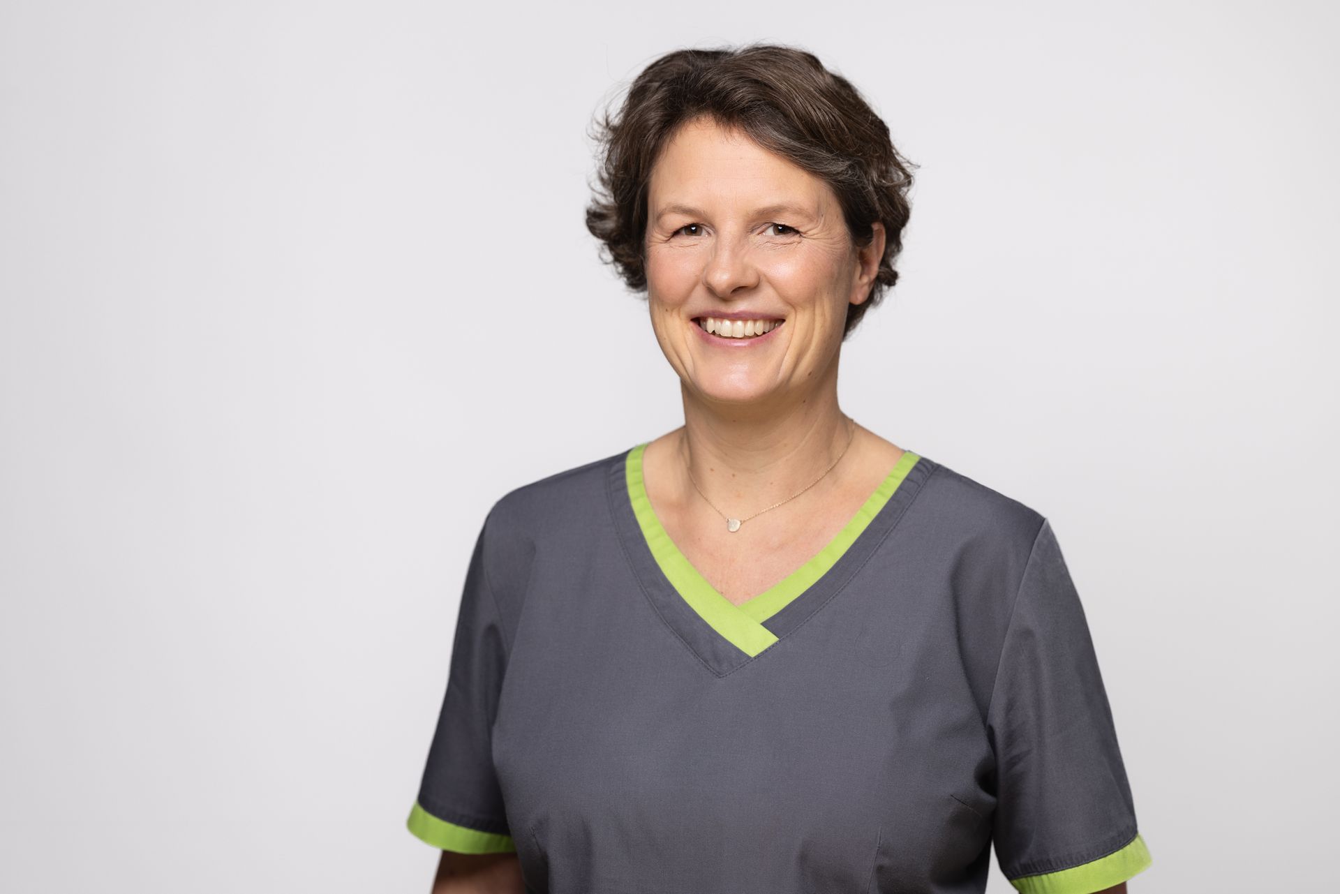 Eine Frau in einem grau - grünen Kasack lächelt in die Kamera.