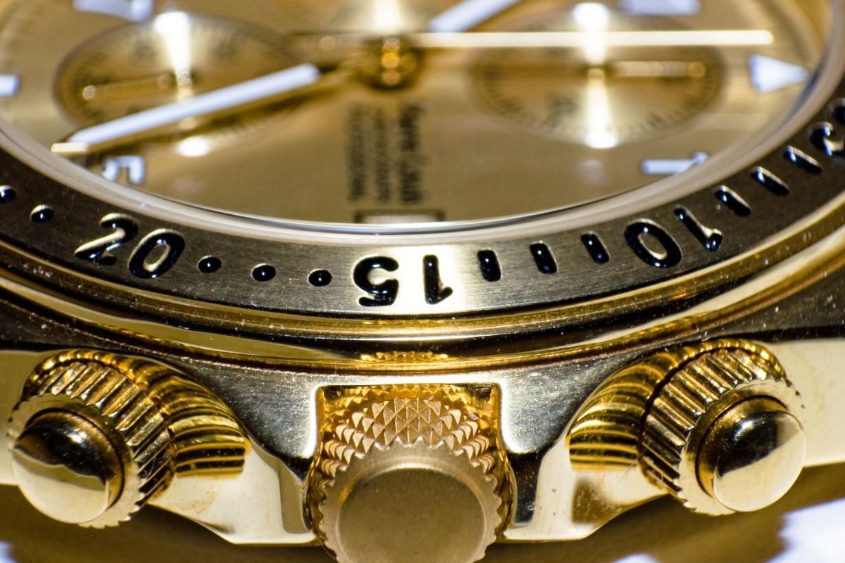Primer plano del bisel y la corona de un reloj de pulsera color oro con números negros grabados.