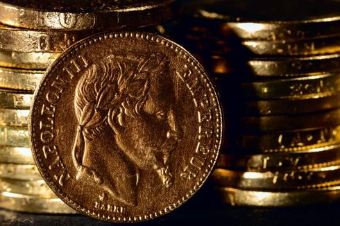 Primer plano de una moneda de oro frente a una pila de monedas de oro.