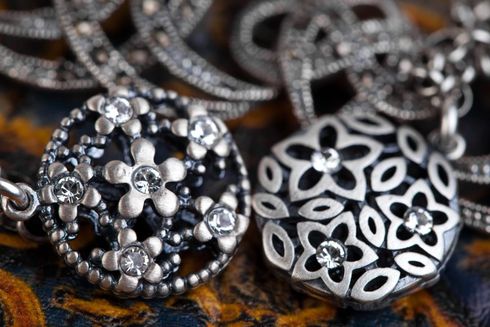 Primer plano de piezas de joyería floral de plata ornamentadas con piedras negras sobre una superficie texturizada.