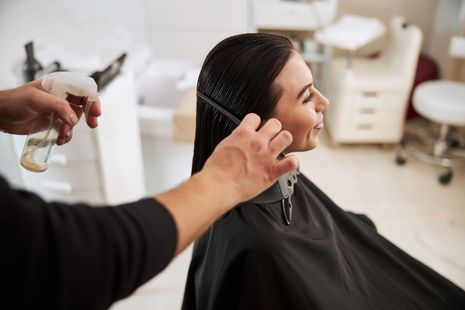 Eine Frau lässt sich in einem Salon von einem Friseur die Haare schneiden.