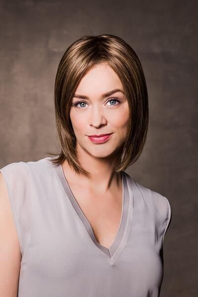 Eine Frau mit Perücke und weißem Hemd schaut in die Kamera.