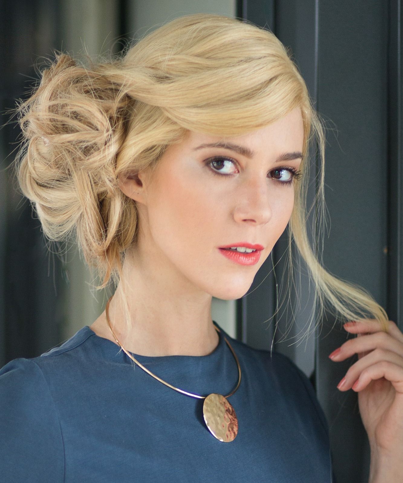 Eine Frau mit blonden Haaren, trägt ein blaues Hemd und eine Halskette