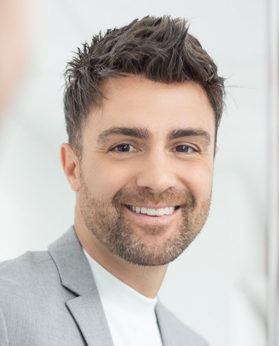 Ein Mann in Anzug und weißem Hemd lächelt in die Kamera