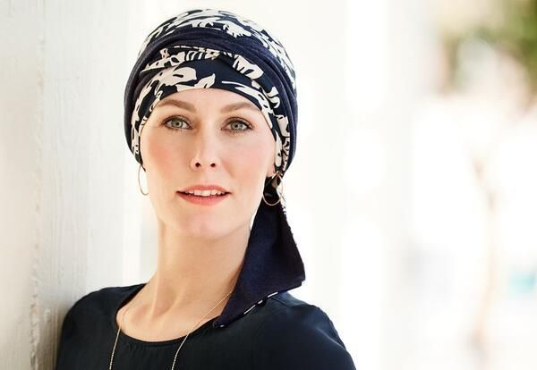 Eine Frau mit Kopftuch und Ohrringen lehnt an einer Wand.