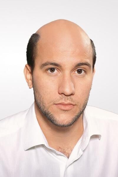 Ein kahlköpfiger Mann mit Bart trägt ein weißes Hemd.