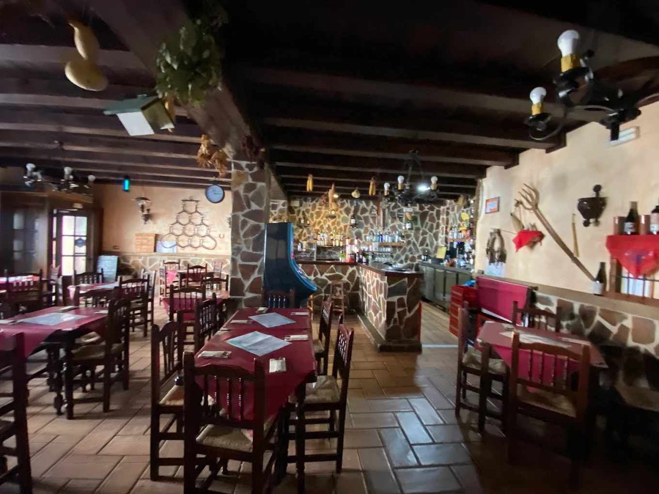 Interior de restaurante rústico con manteles rojos, sillas de madera y paredes de piedra.