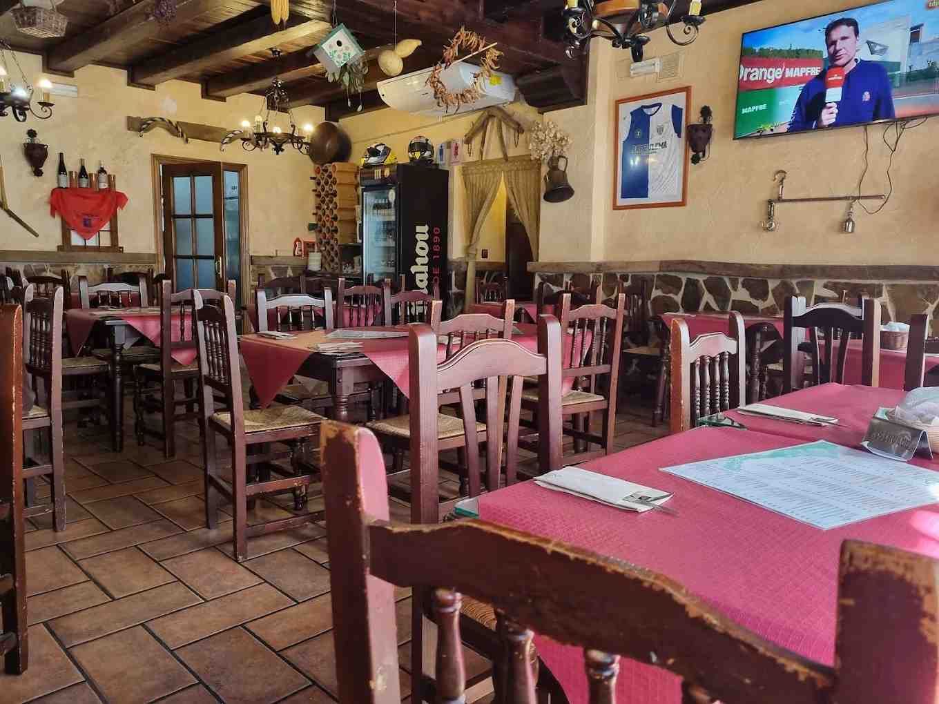 Interior de restaurante con mesas y sillas de madera, paredes de piedra y suelo de baldosas.