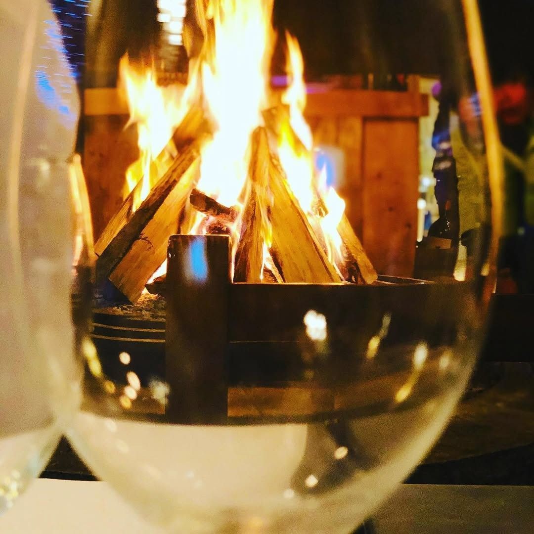 Una copa de vino frente a una chimenea crepitante con cálidas llamas anaranjadas.
