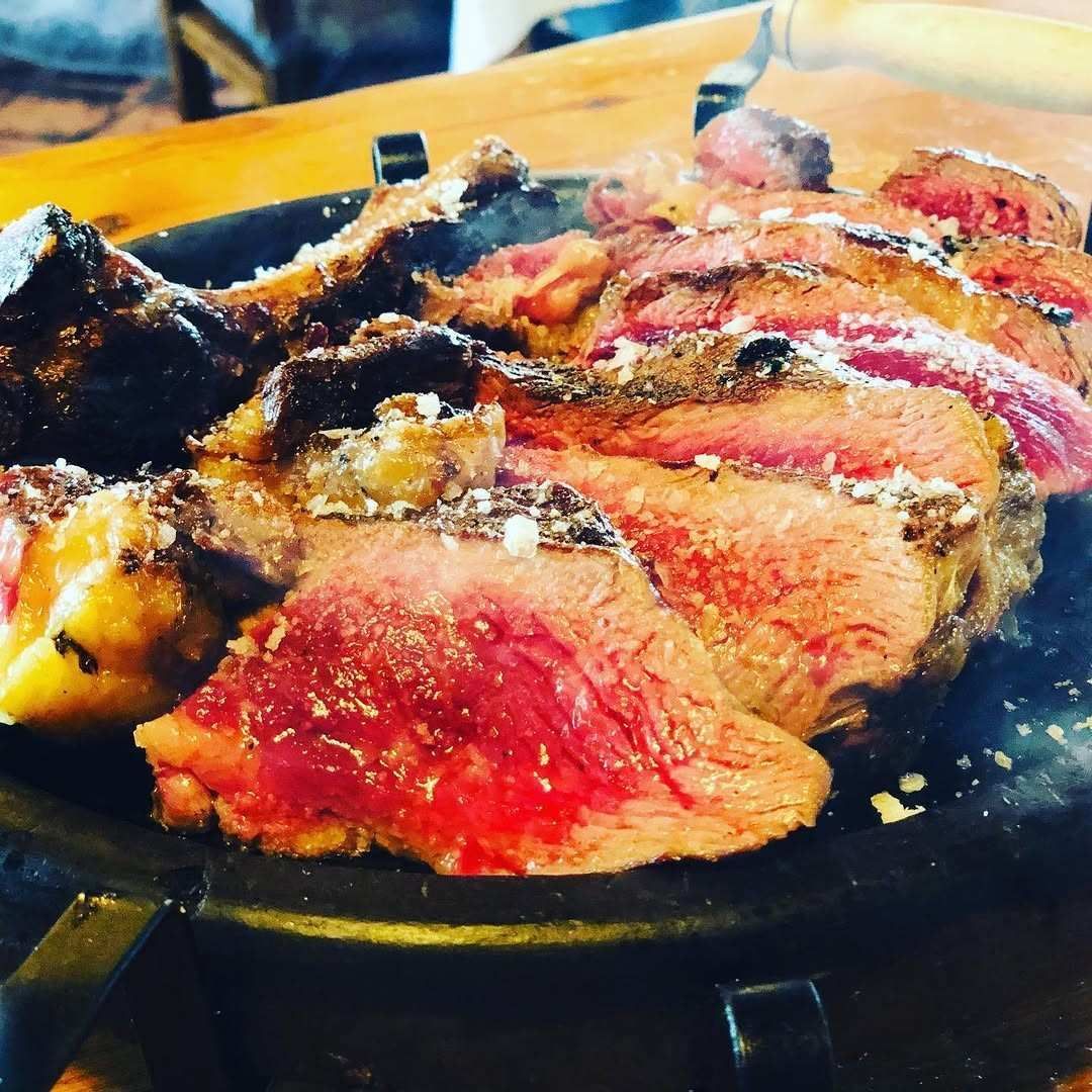 Filete sellado en rodajas sobre un plato negro, cubierto con salsa y pan rallado, sobre una mesa de madera.