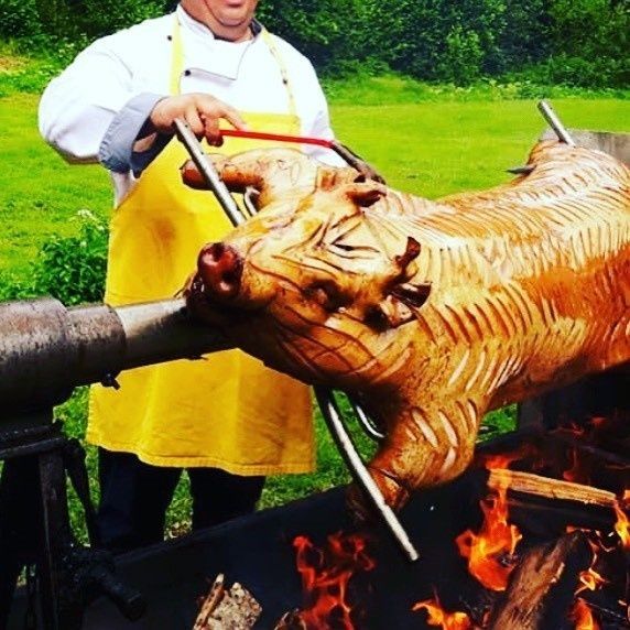 Un chef asa un cerdo entero al espetón sobre una hoguera al aire libre.