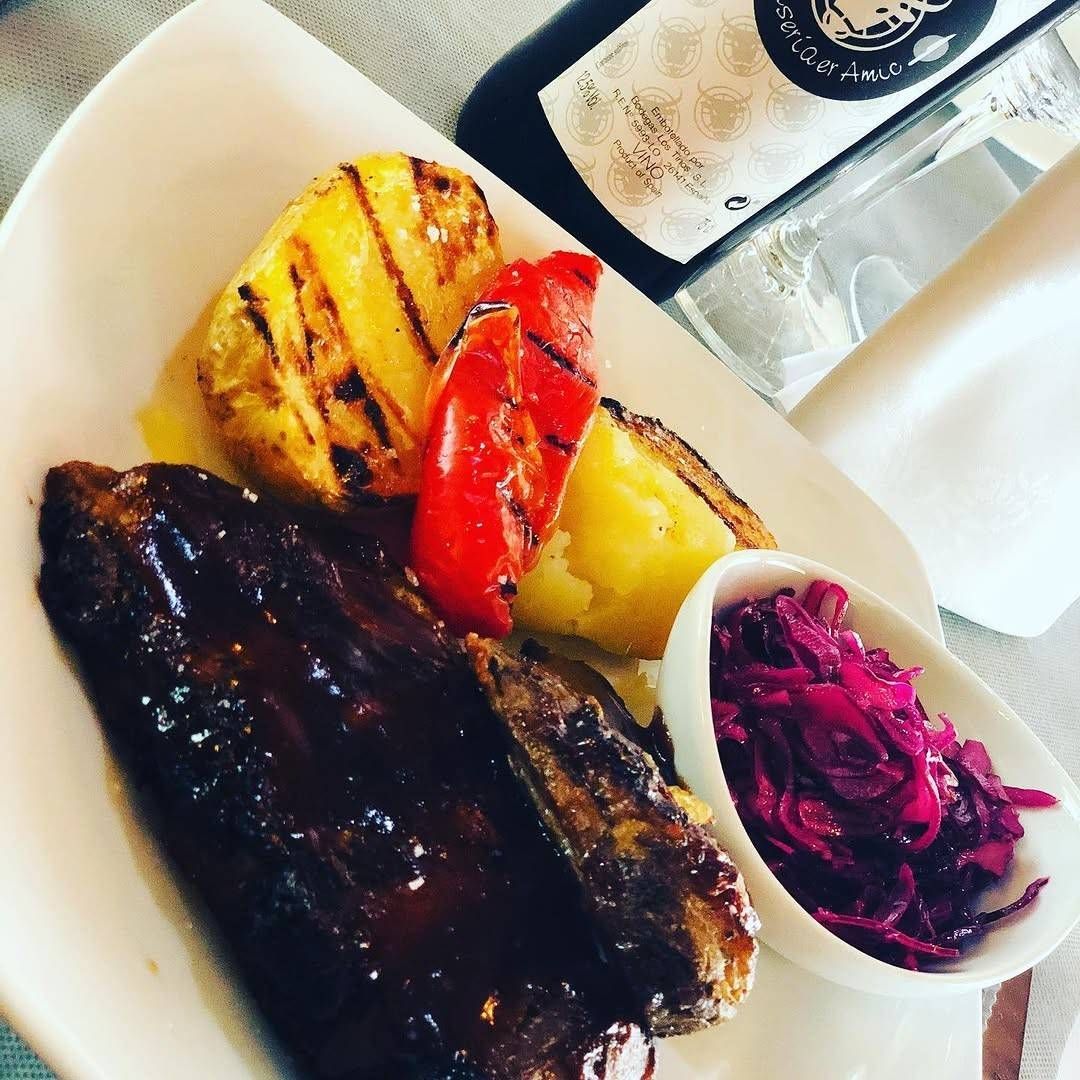 Filete a la parrilla emplatado con verduras asadas y ensalada de col morada acompañada de una salsa para mojar.