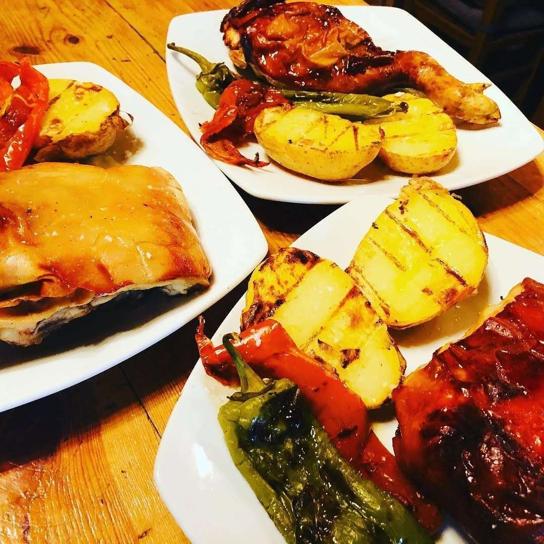 Platos de pollo asado y patatas sobre una mesa de madera, acompañados de judías verdes y pimientos rojos.