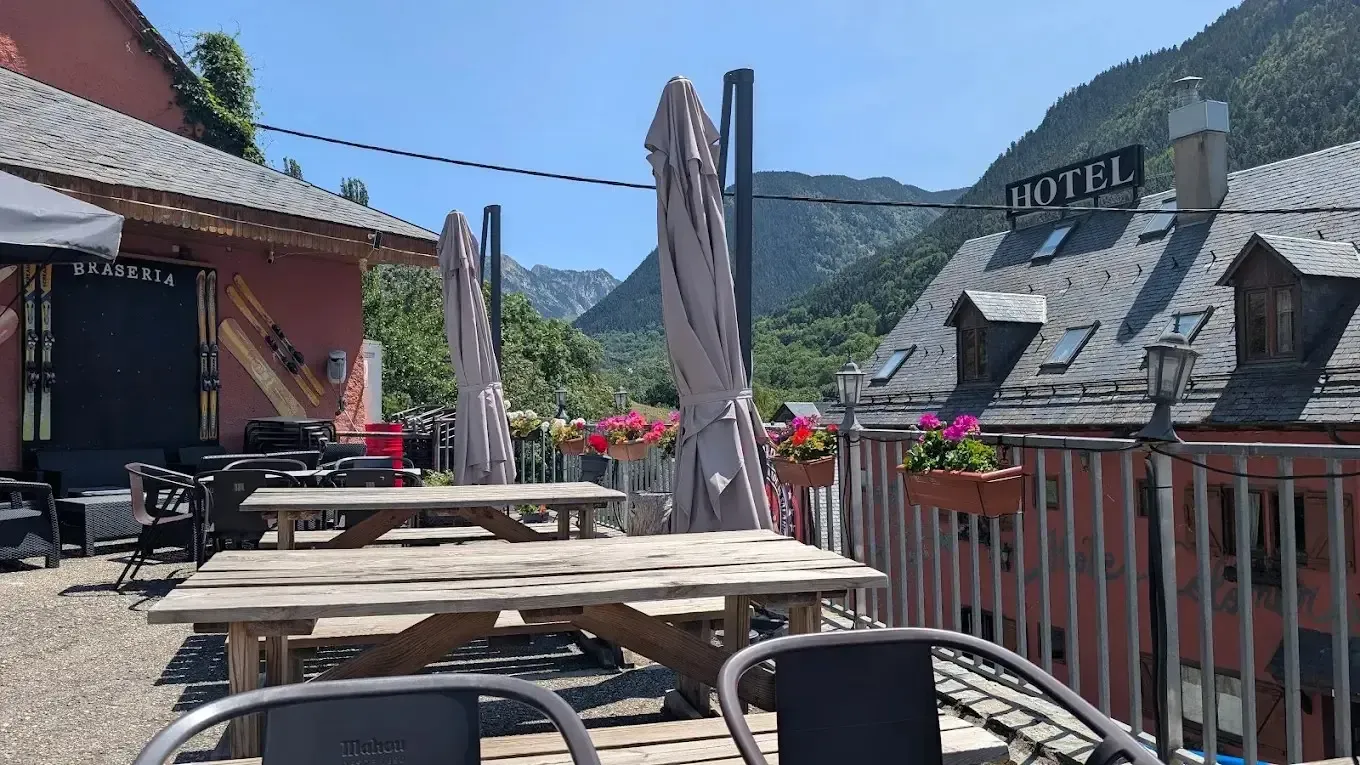Terraza soleada de un café de montaña con mesas de madera, flores rojas y tejados de hoteles al fondo.