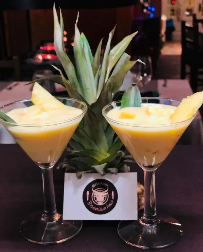 Dos cócteles de piña en copas de martini con un centro de mesa de piña sobre una mesa de bar.