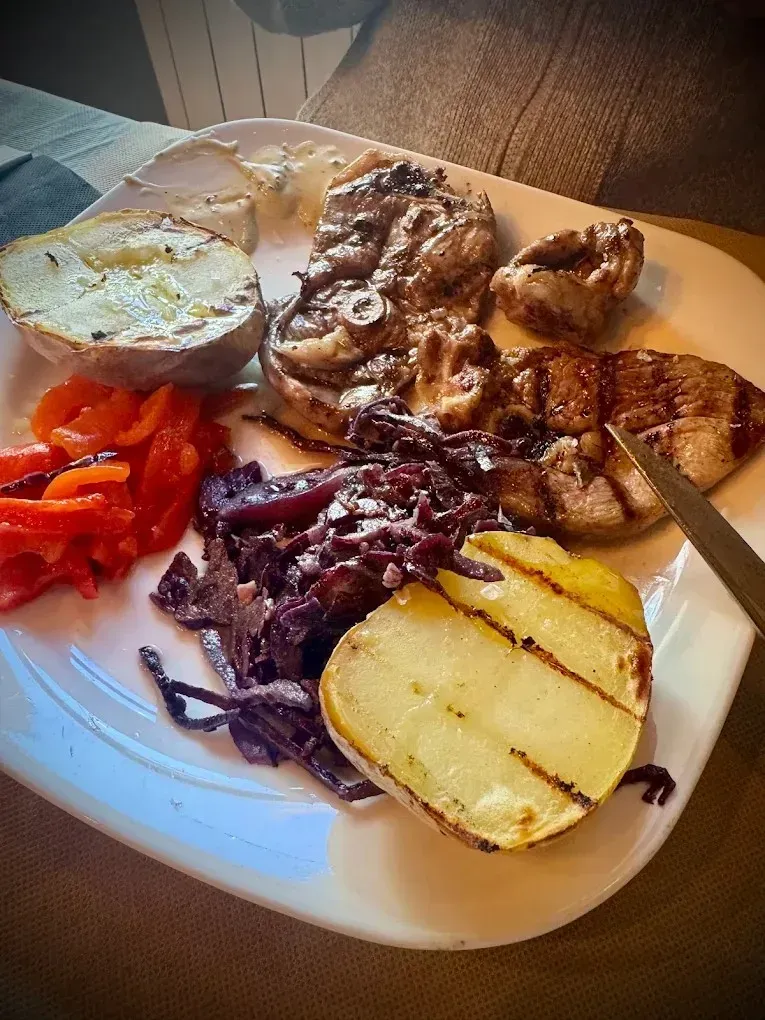 Plato con carne a la parrilla, patata asada, cebollas, tomates, col lombarda y un huevo frito con una rodaja de limón.
