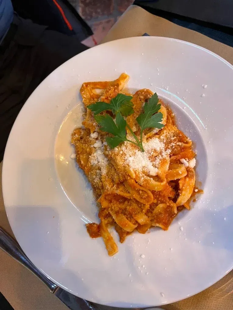 Pasta con salsa roja y queso rallado, adornada con albahaca, servida en un plato blanco.