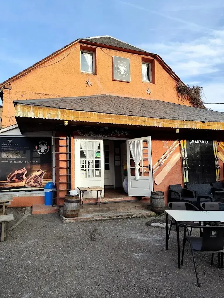 Pub o cafetería con techo naranja, con mesas y sillas al aire libre en un patio de grava.