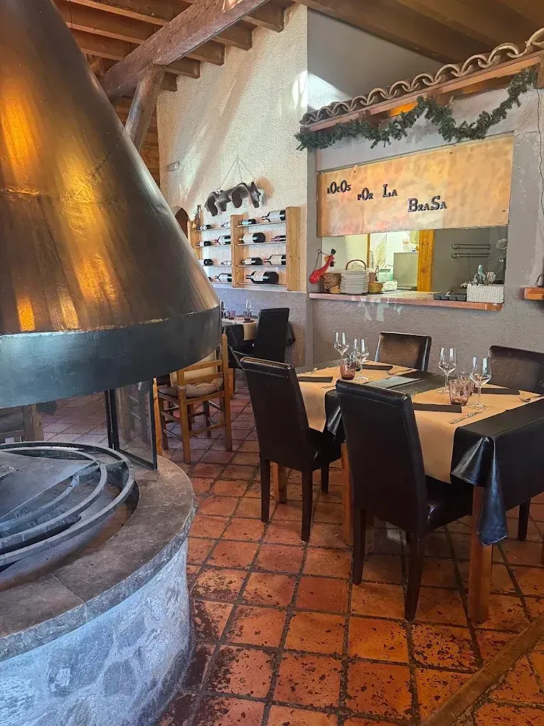 Acogedor comedor de restaurante con una gran chimenea, sillas negras, manteles a cuadros y suelo de baldosas.