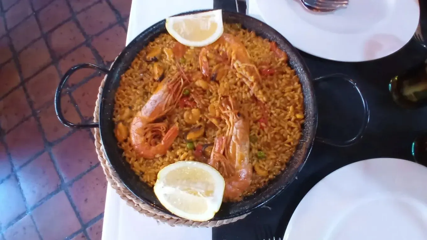 Paella de gambas en una sartén negra, adornada con rodajas de limón sobre una mesa de comedor.