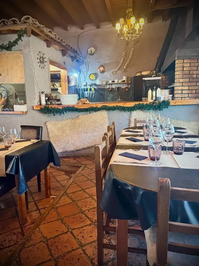 Acogedor comedor de restaurante rústico con mesas puestas, suelo de ladrillo y cálida iluminación de araña.