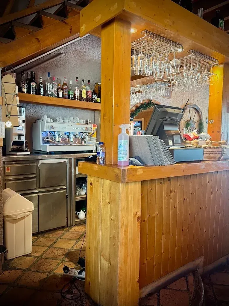 Barra cálida con paneles de madera, botellas, vasos colgantes y una caja registradora bajo vigas a la vista.