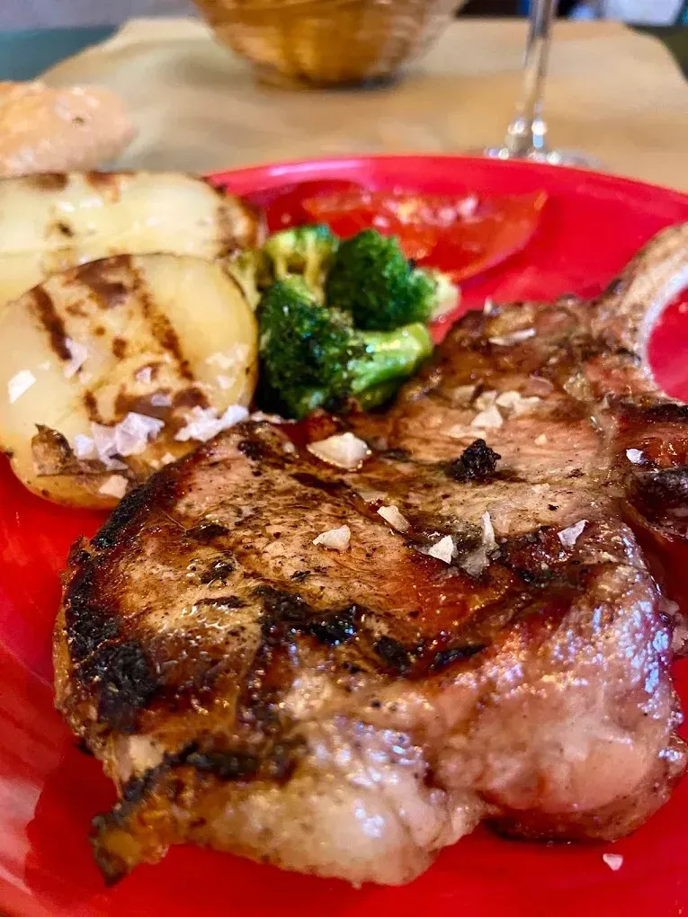 Filete a la parrilla con patatas asadas y brócoli en un plato rojo.