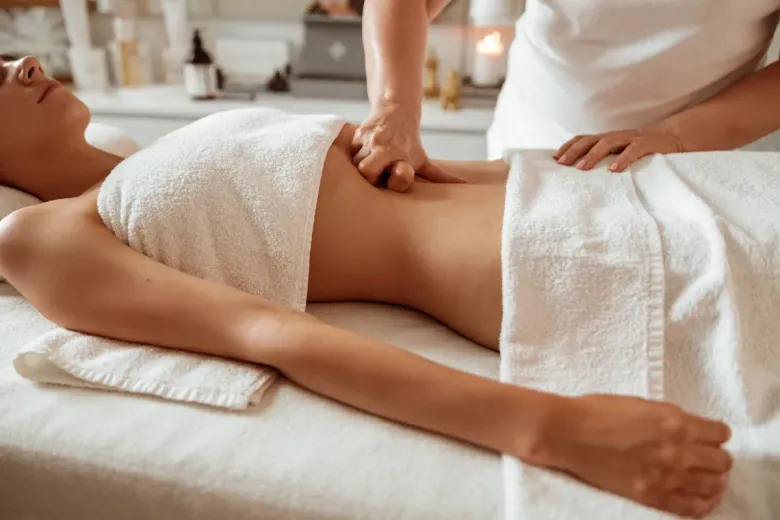 Persona recibiendo masaje abdominal, acostada sobre una mesa de masajes, cubierta con una toalla blanca.