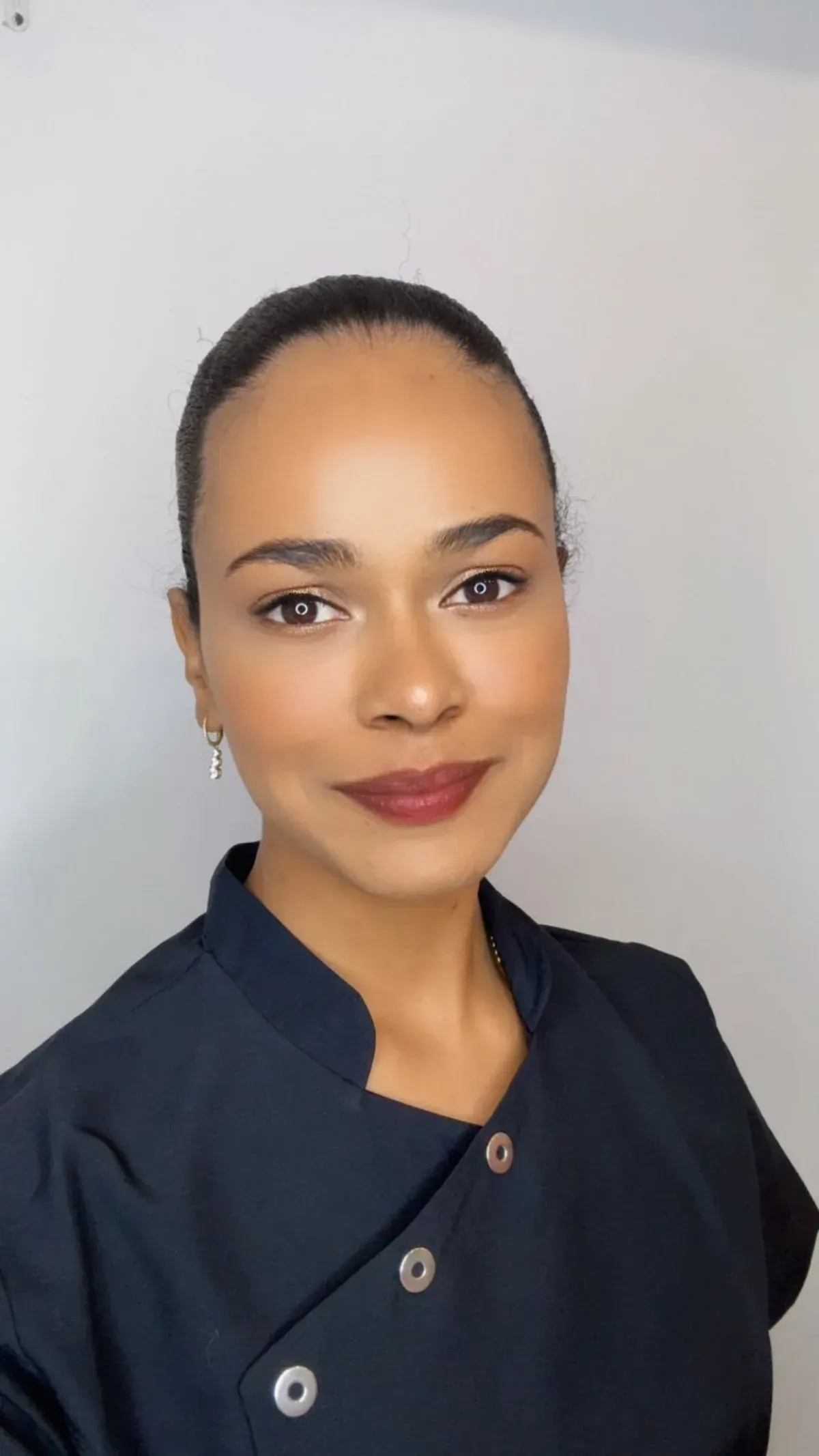 Una mujer con uniforme azul oscuro sonríe, mirando directamente a la cámara. Fondo neutro.