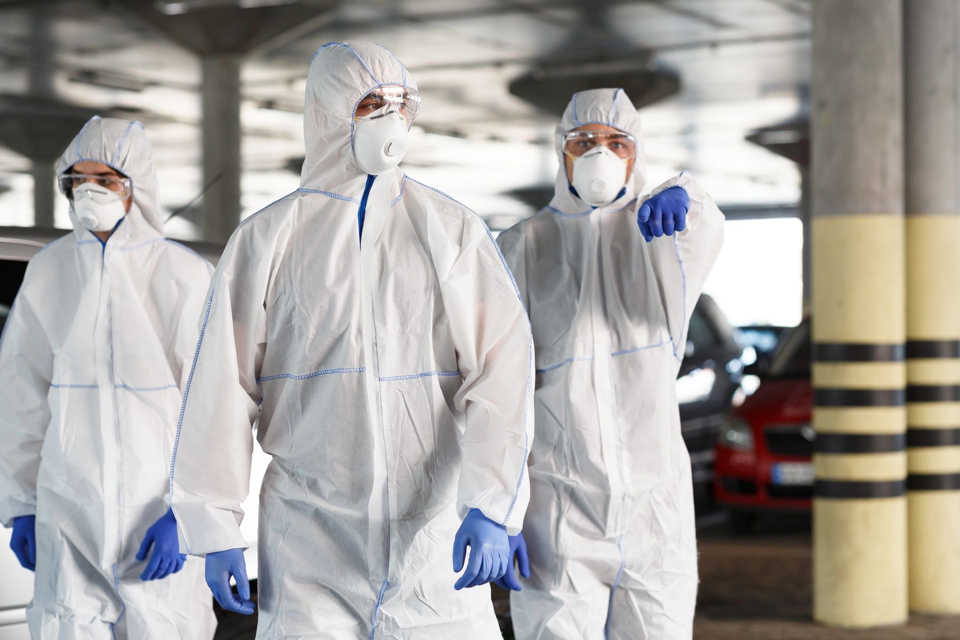 Tres personas con trajes protectores y máscaras caminan en un estacionamiento.