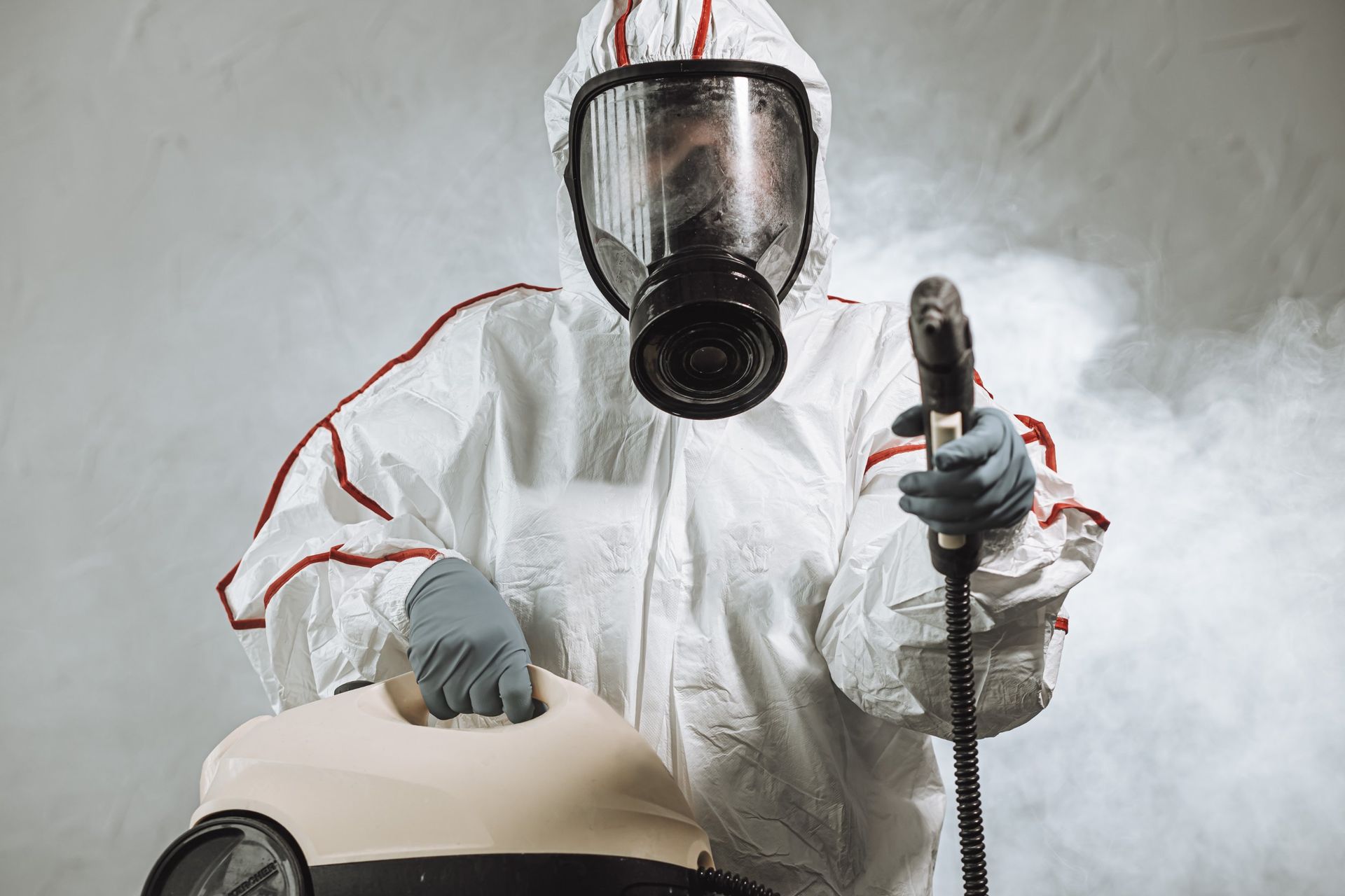 Un hombre con traje de protección y máscara de gas sostiene una aspiradora.