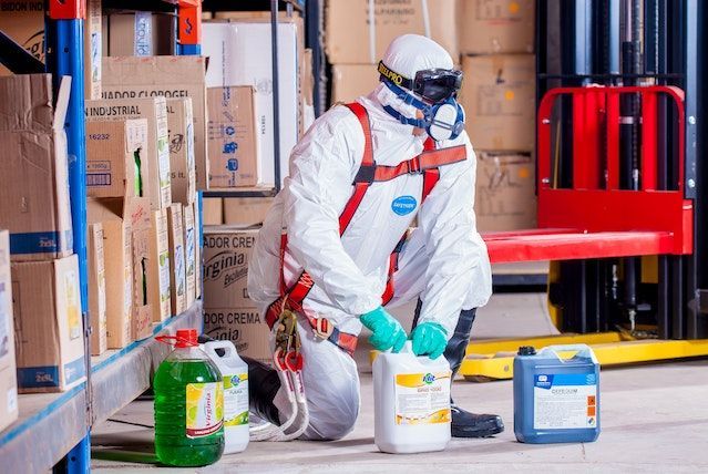 Un hombre con un traje de protección está arrodillado en un almacén con botellas de productos químicos.