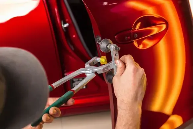 Un hombre está trabajando en la puerta de un coche rojo con un par de alicates.