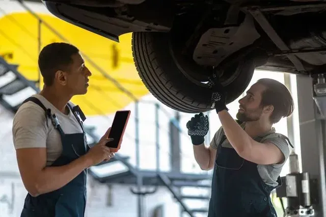 Dos mecánicos están trabajando en los bajos de un coche en un garaje.