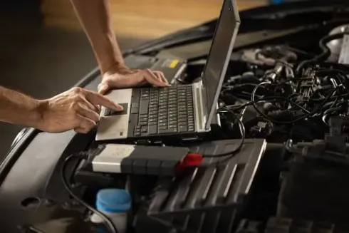 Una persona está usando una computadora portátil debajo del capó de un automóvil.