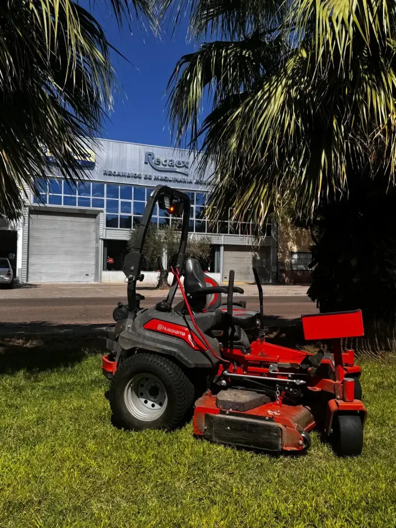 Cortacésped rojo sobre el césped bajo palmeras frente a un edificio.