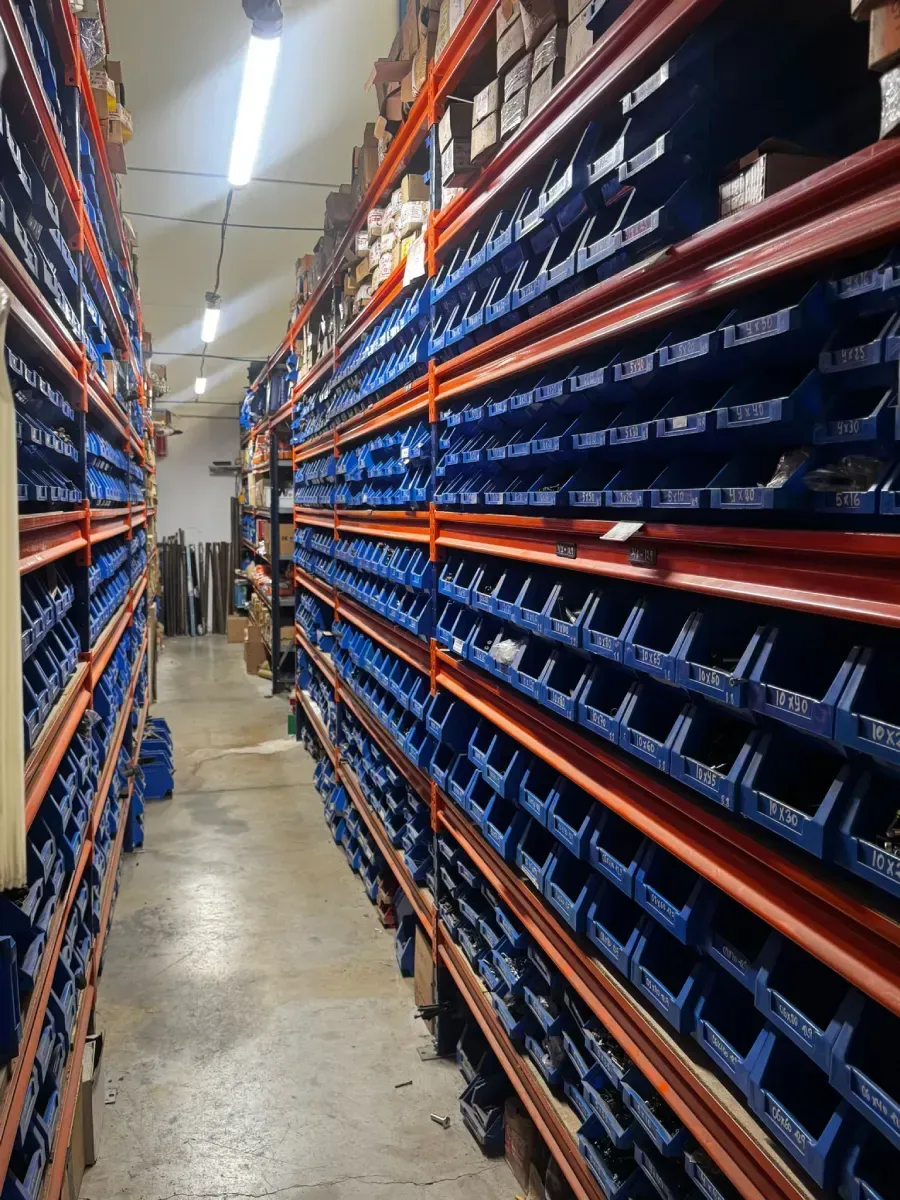 Pasillo de un almacén repleto de estanterías altas de color naranja y contenedores de almacenamiento azules, iluminados con luces brillantes desde el techo.