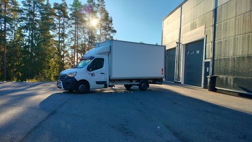 Moderni valkoinen talo mustilla yksityiskohdilla ja puisella terassilla, sininen taivas yläpuolella.