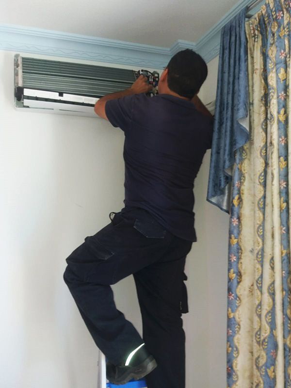 Un hombre con una camisa negra está trabajando en un aire acondicionado.