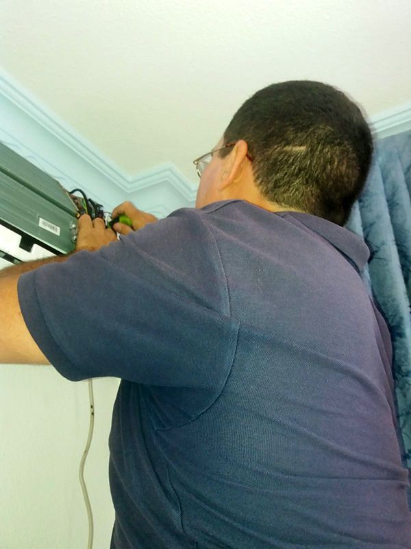 Un hombre con una camisa azul está trabajando en un aire acondicionado.