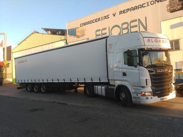 Un camión semirremolque blanco está estacionado frente a un edificio que dice feioben