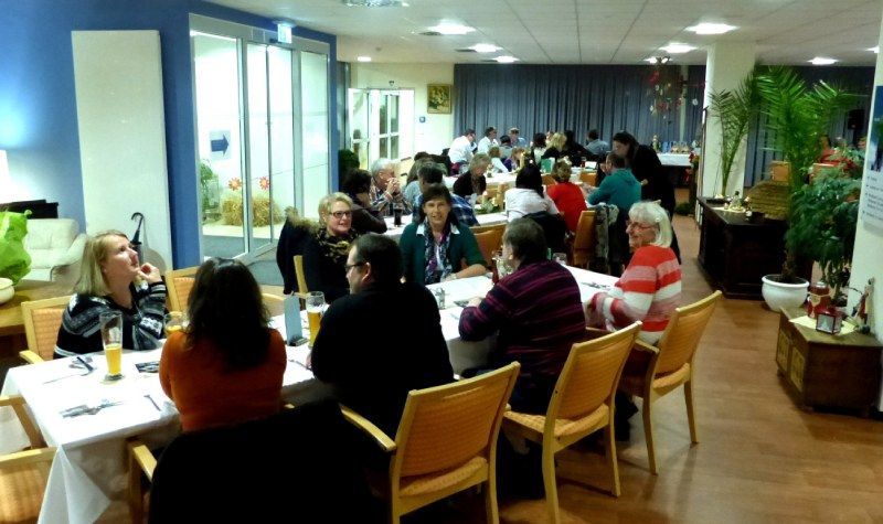 Menschen sitzen an Tischen in einem hellen Speisesaal, unterhalten sich und essen.
