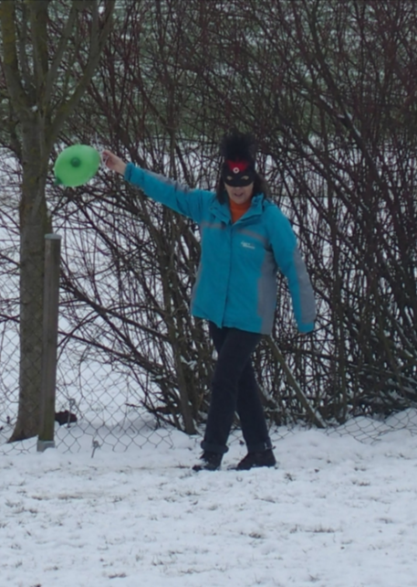 Person in blauer Jacke, die einen grünen Ballon im Freien in einem verschneiten Wald hält