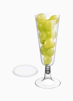 Copa de champán de plástico transparente llena de uvas verdes; tapa al lado.