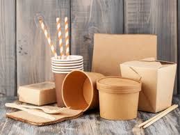 Surtido de recipientes para alimentos, vasos, pajitas y utensilios de papel marrón desechables sobre una superficie de madera.