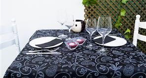 Mesa puesta para dos con platos, vasos y elementos decorativos sobre mantel paisley negro.